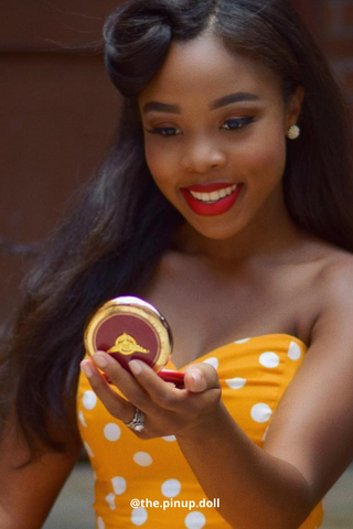 Woman wearing a yellow polka dot dress and red lipstick holding a compact powder